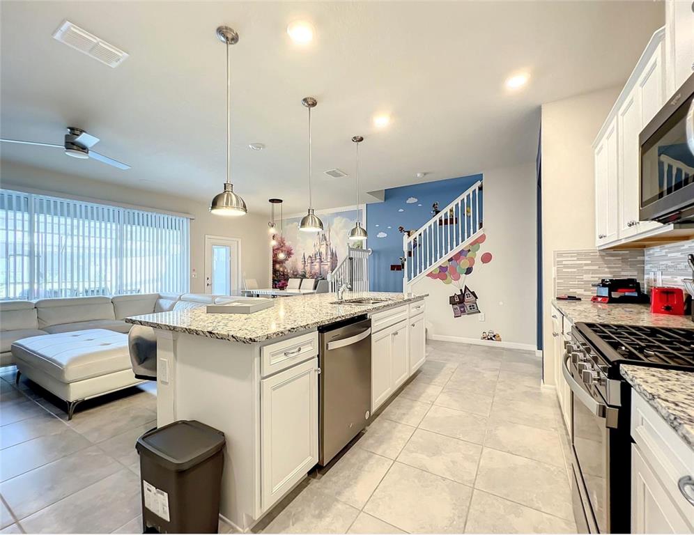 A kitchen with white cabinets, granite countertops, and a staircase featuring a mural wall — 7108 OAKMOSS LOOP, DAVENPORT, FL