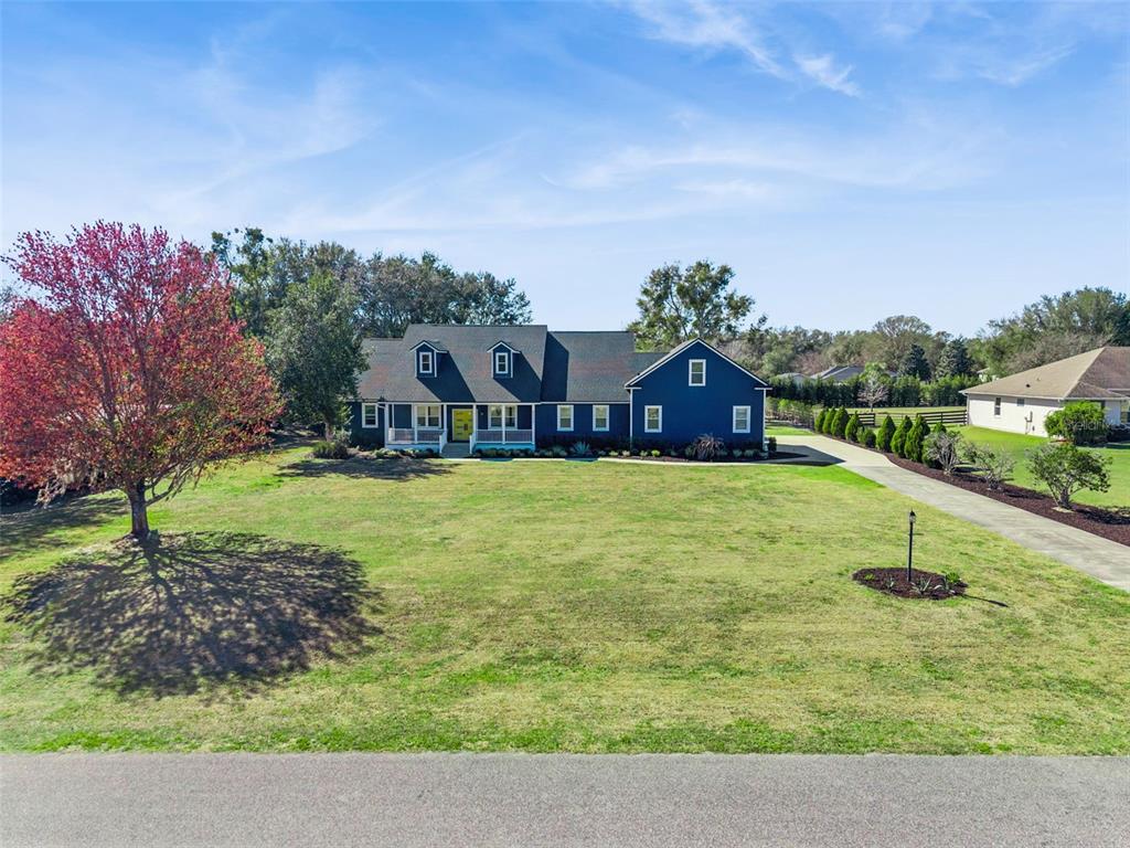 A two-story dark blue house with a front porch sits on a large grassy lot — 32345 WOLFS TRAIL, SORRENTO, FL