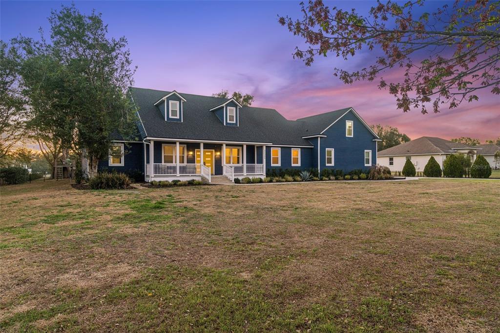 A two-story blue house with a front porch and dormer windows sits on a lawn — 32345 WOLFS TRAIL, SORRENTO, FL