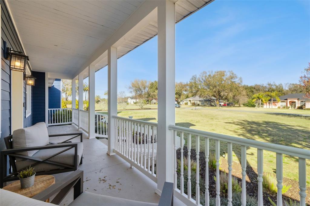 A covered porch features white railings, support columns, and outdoor seating overlooking a grassy yard — 32345 WOLFS TRAIL, SORRENTO, FL