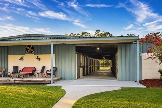 A metal-sided horse barn features a covered porch with outdoor seating and a concrete walkway — 16525 SW 5TH PLACE, NEWBERRY, FL