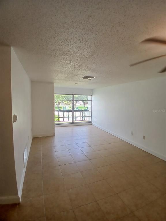 An empty room with white walls, beige tile flooring, a ceiling fan, and a large window — 2700 BAYSHORE BOULEVARD UNIT 2211, DUNEDIN, FL