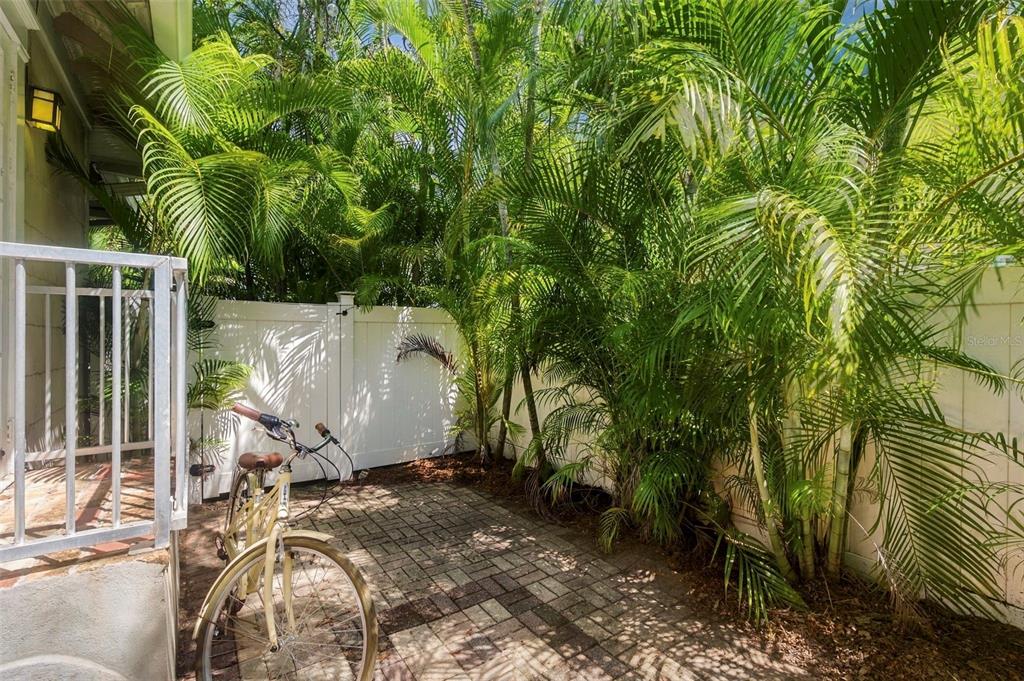 A paved patio area features a bicycle, white vinyl fencing, and lush palm trees — 406 10TH AVENUE NE, ST PETERSBURG, FL