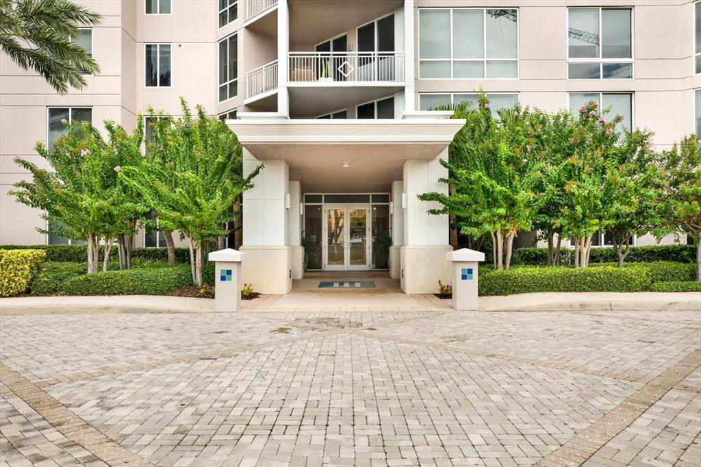 The exterior entrance of a multi-story building features a paved driveway and landscaped trees — 331 CLEVELAND STREET UNIT 212, CLEARWATER, FL