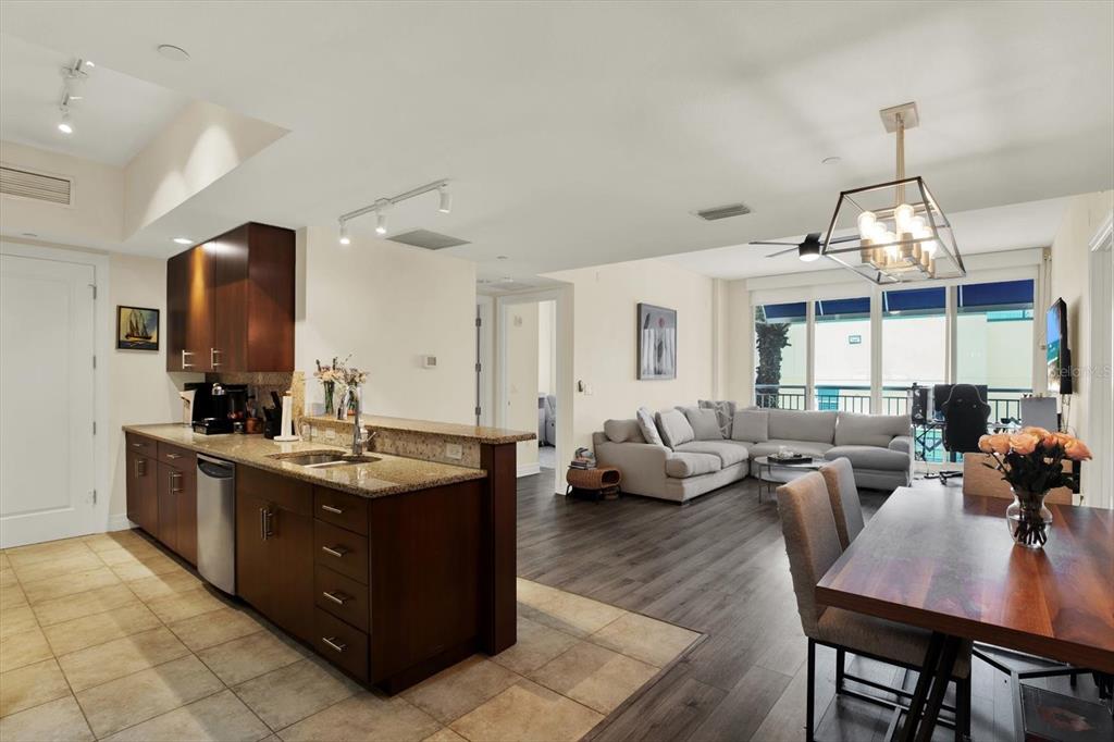 An open-concept kitchen with dark wood cabinets and granite countertops overlooks a living and dining area — 331 CLEVELAND STREET UNIT 212, CLEARWATER, FL