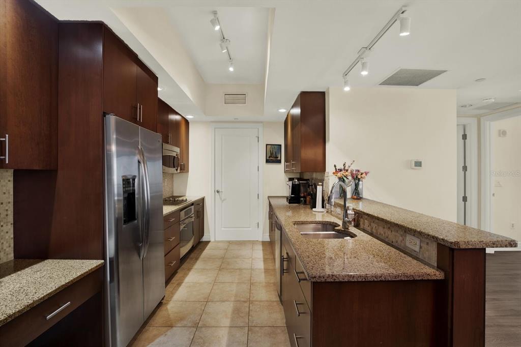 A kitchen features dark wood cabinets, granite countertops, stainless steel appliances, and tile flooring — 331 CLEVELAND STREET UNIT 212, CLEARWATER, FL