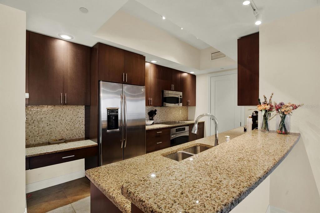 A kitchen features dark wood cabinets, granite countertops, stainless steel appliances, and a tiled backsplash — 331 CLEVELAND STREET UNIT 212, CLEARWATER, FL