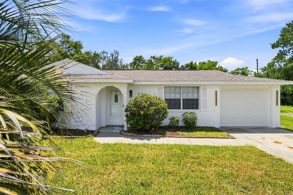 A single-story white house with a front-facing garage and a small arched entryway — 6214 WESTPORT DRIVE, PORT RICHEY, FL