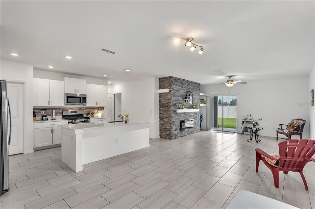 An open-concept kitchen and living area featuring white cabinetry, a stone fireplace, and tile flooring — 22547 STORYBOOK CABIN WAY, LAND O LAKES, FL