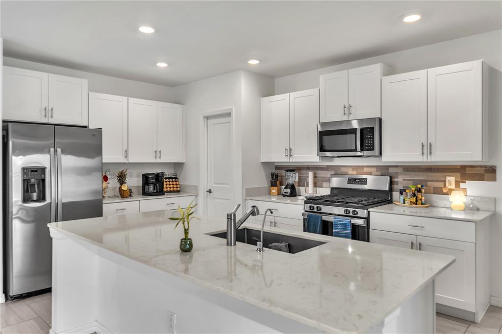 A modern kitchen features white cabinets, stainless steel appliances, and a large quartz-topped island — 22547 STORYBOOK CABIN WAY, LAND O LAKES, FL