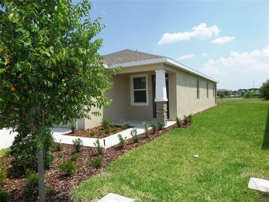 A tan stucco house with a stone-based porch column and a landscaped front yard — 5039 STOKES WAY, WILDWOOD, FL
