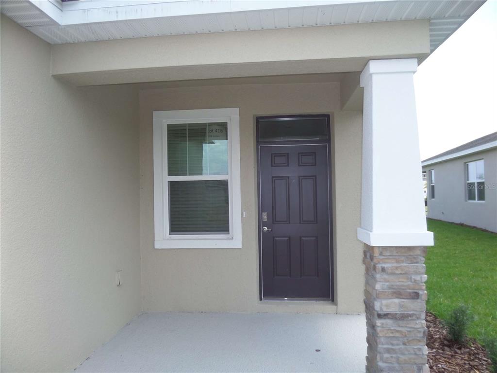 A covered front porch features a dark door, a single window, and a stone-based pillar — 5039 STOKES WAY, WILDWOOD, FL