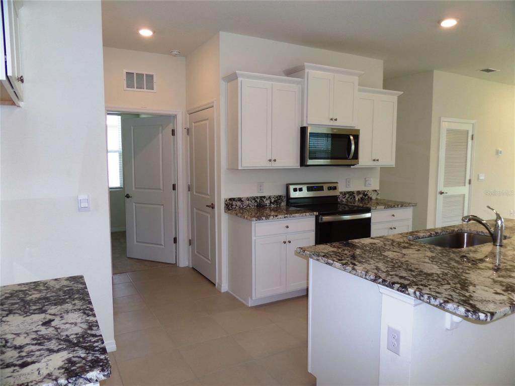 A kitchen features white cabinets, granite countertops, a stainless steel microwave, and a center island — 5039 STOKES WAY, WILDWOOD, FL