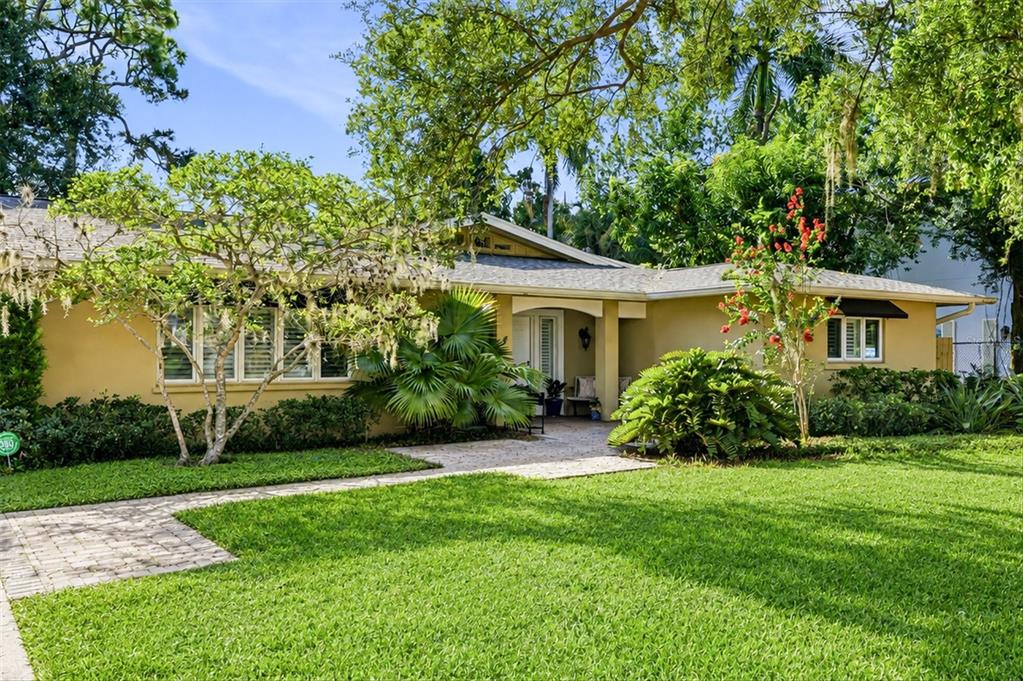 A single-story house with yellow siding, a stone walkway, and lush landscaping under a blue sky — 1041 CITRUS AVENUE, SARASOTA, FL