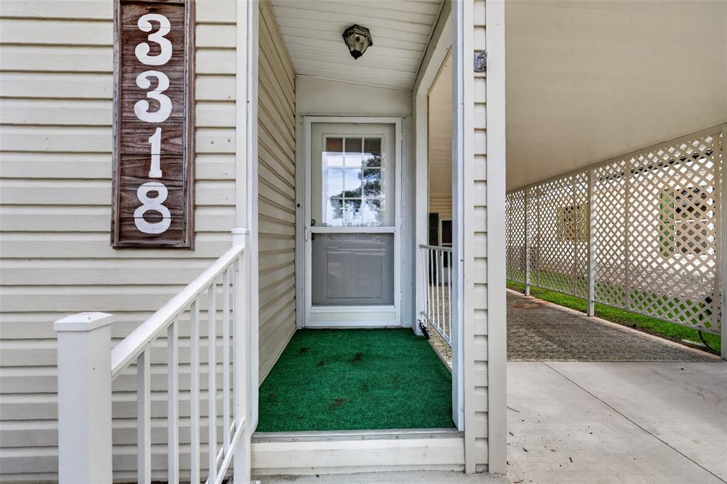 A house entrance features a green mat, a storm door, and a vertical address sign — 3318 WEKIVA ROAD, TAVARES, FL