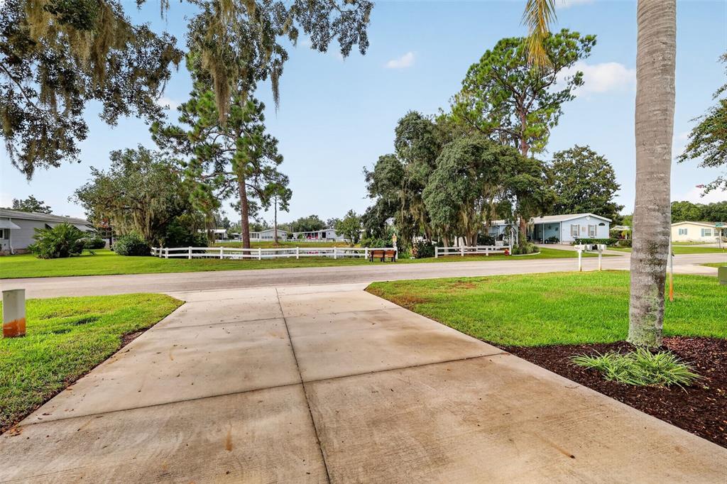 A concrete driveway leads toward a residential street lined with trees and mobile homes — 3318 WEKIVA ROAD, TAVARES, FL