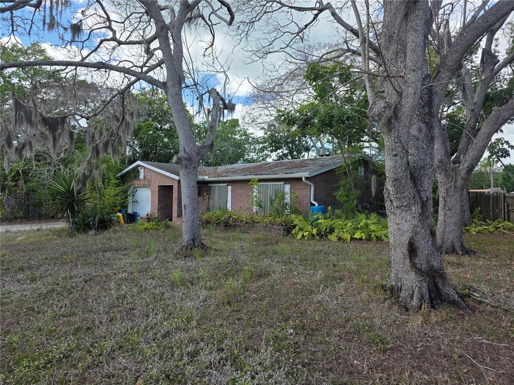 A single-story brick house with a garage sits behind large trees on a grassy lot — 1016 GREER DRIVE, SARASOTA, FL