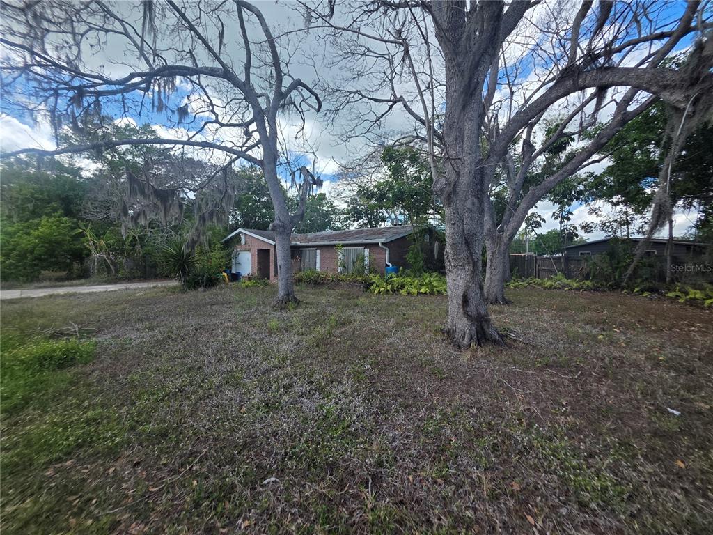 A single-story brick house sits behind large trees on a grassy lot — 1016 GREER DRIVE, SARASOTA, FL
