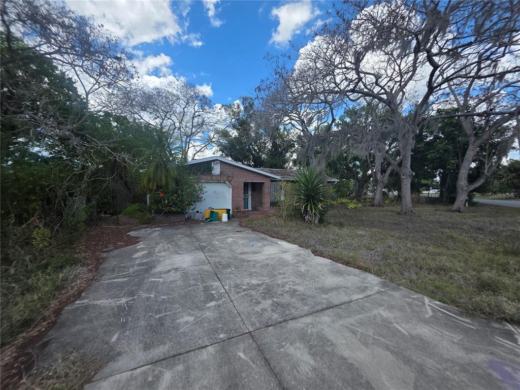 A single-story brick house with a concrete driveway and mature trees in the yard — 1016 GREER DRIVE, SARASOTA, FL