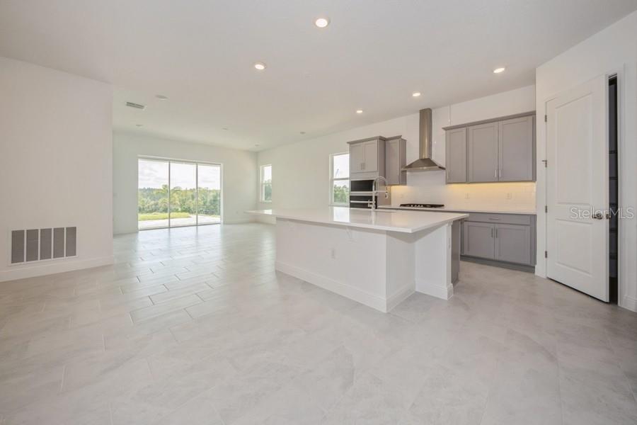 A modern kitchen with gray cabinets and a white island opens to a living area — 16029 VOLTERRA POINT, MONTVERDE, FL