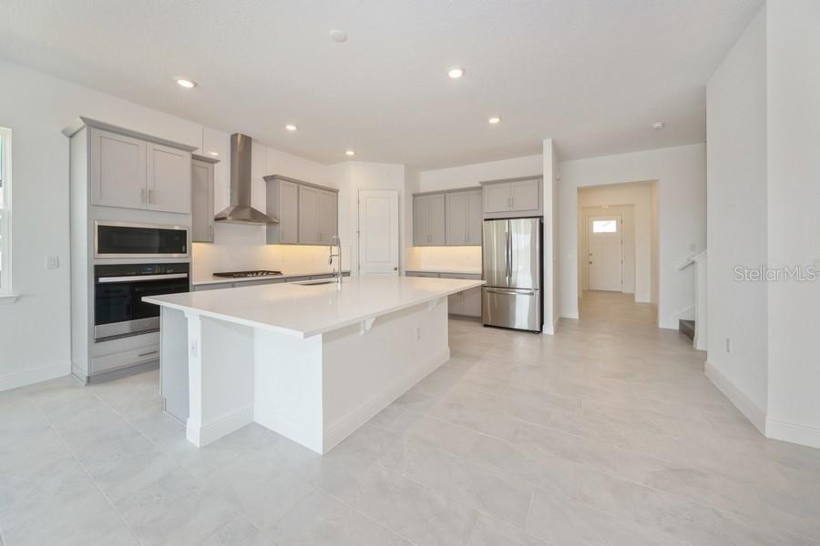 A modern kitchen features light gray cabinetry, a large white island, and stainless steel appliances — 16029 VOLTERRA POINT, MONTVERDE, FL
