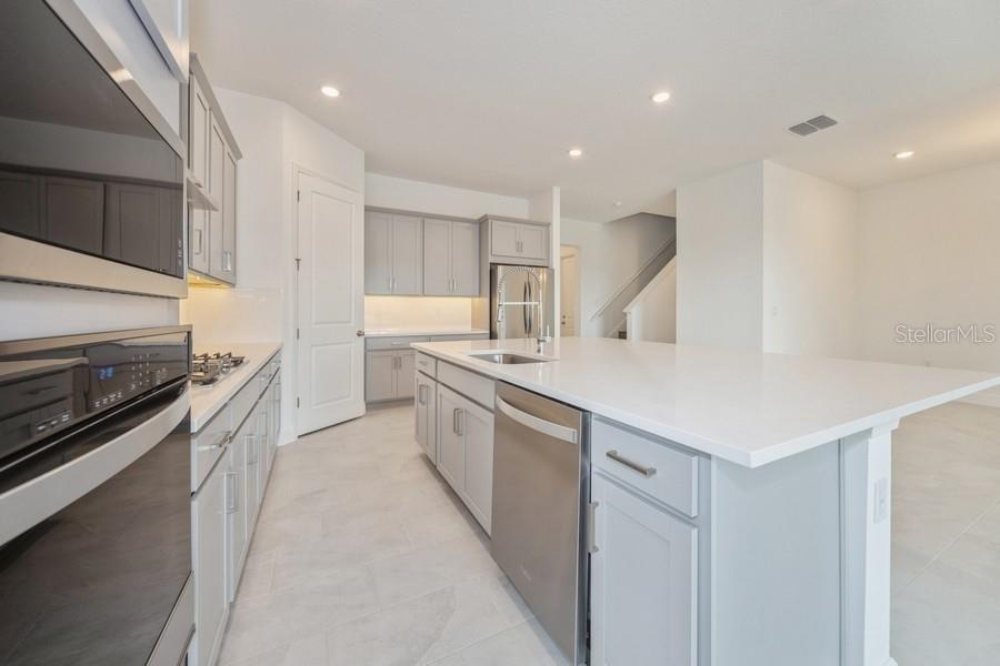 A modern kitchen features gray cabinets, white countertops, stainless steel appliances, and tile flooring — 16029 VOLTERRA POINT, MONTVERDE, FL