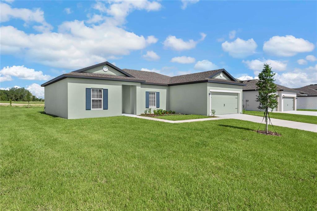 A single-story house with light green stucco siding, a two-car garage, and a grassy lawn — 628 TANGELO TERRACE, BABSON PARK, FL
