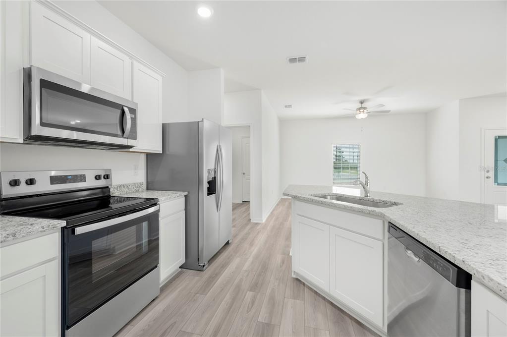 A modern kitchen features white cabinets, stainless steel appliances, and a granite-topped island — 628 TANGELO TERRACE, BABSON PARK, FL