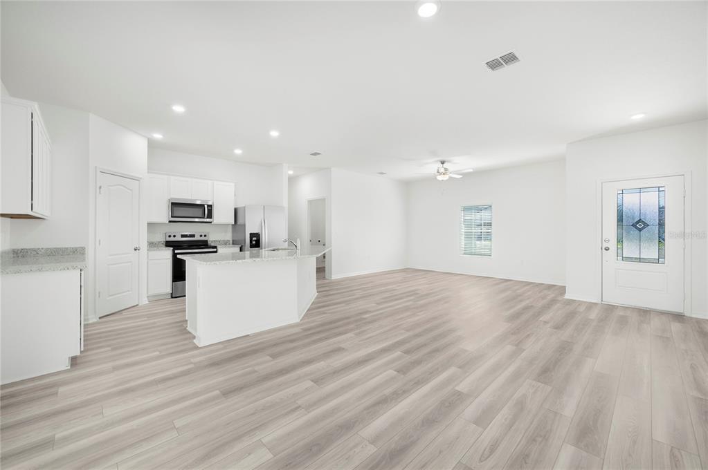 An open-concept kitchen and living area features white cabinetry, stainless appliances, and light wood flooring — 628 TANGELO TERRACE, BABSON PARK, FL