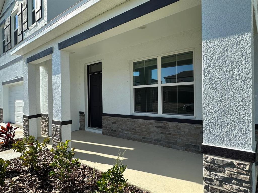 A covered porch features a dark front door, stone veneer accents, and a large window — 12760 LATERAL ROOT DRIVE, SARASOTA, FL