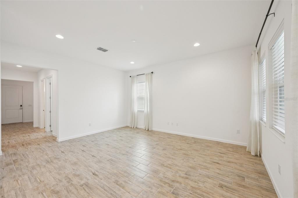 A bright, empty room features light wood-look tile flooring, white walls, and multiple windows — 806 WINTERSIDE DRIVE, APOLLO BEACH, FL