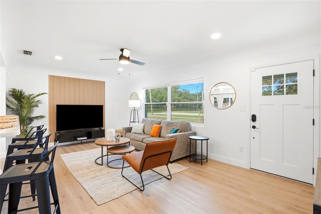 A living room features light wood floors, a slatted wood accent wall, and a gray sofa — 2117 N HERCULES AVENUE, CLEARWATER, FL