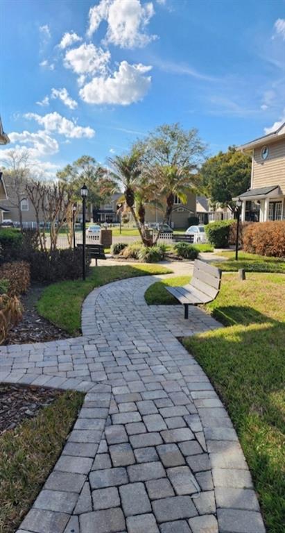 A paved walkway winds through a landscaped courtyard with benches, palm trees, and residential buildings — 6050 SCOTCHWOOD GLEN UNIT 105, ORLANDO, FL