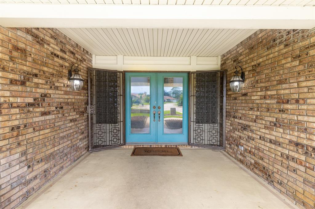 A covered brick porch features a teal double front door with decorative metal security screens — 82 KINGSLEY PLACE, ORMOND BEACH, FL