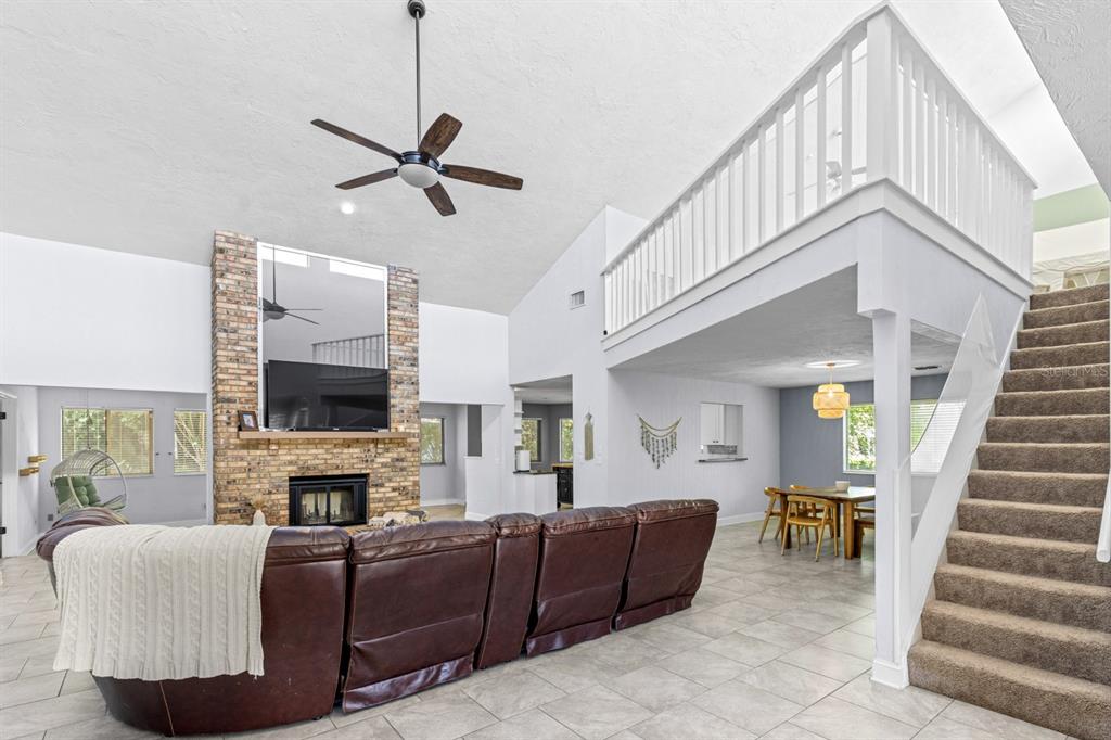 A living room with a brick fireplace, vaulted ceiling, loft area, and carpeted stairs — 82 KINGSLEY PLACE, ORMOND BEACH, FL