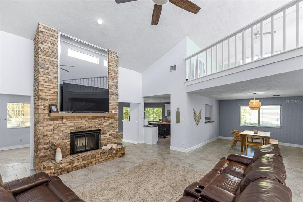 A living room with a brick fireplace, vaulted ceiling, loft railing, and tile flooring — 82 KINGSLEY PLACE, ORMOND BEACH, FL