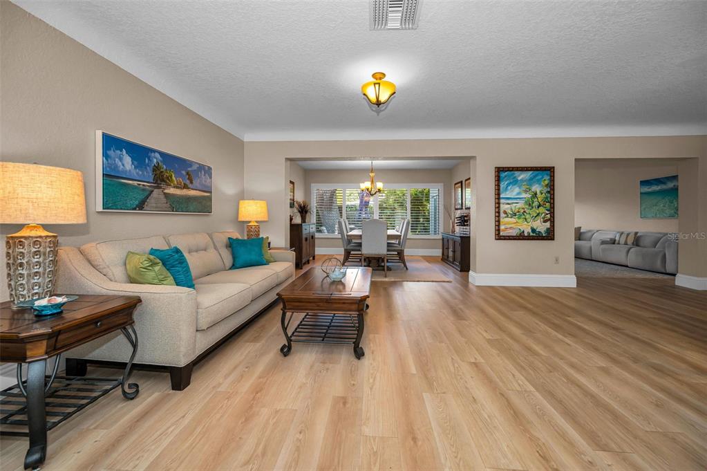 A living room with light wood flooring, a beige sofa, and an adjacent dining area — 1732 GOLF VIEW DRIVE, BELLEAIR, FL
