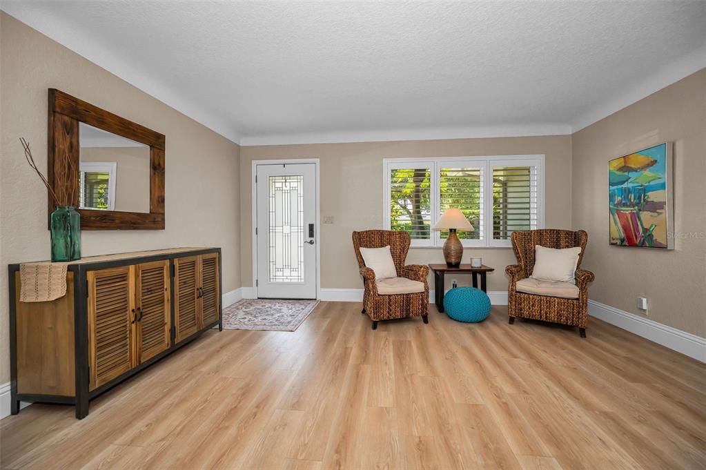 A living room features light wood flooring, two wicker chairs, and a wooden console table — 1732 GOLF VIEW DRIVE, BELLEAIR, FL
