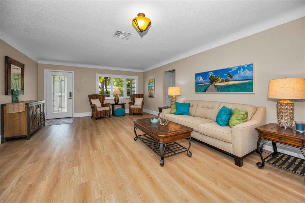 A living room features light wood flooring, a beige sofa, and a tropical wall art piece — 1732 GOLF VIEW DRIVE, BELLEAIR, FL