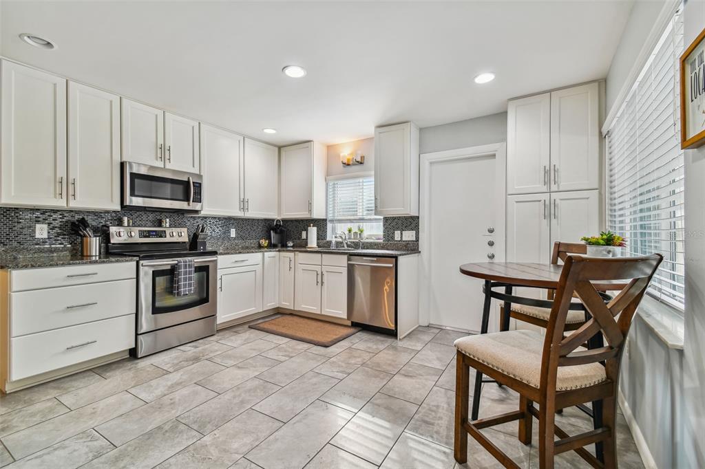 A kitchen features white cabinets, stainless steel appliances, a tiled backsplash, and a small dining area — 1523 BAYSHORE BOULEVARD UNIT 6, DUNEDIN, FL