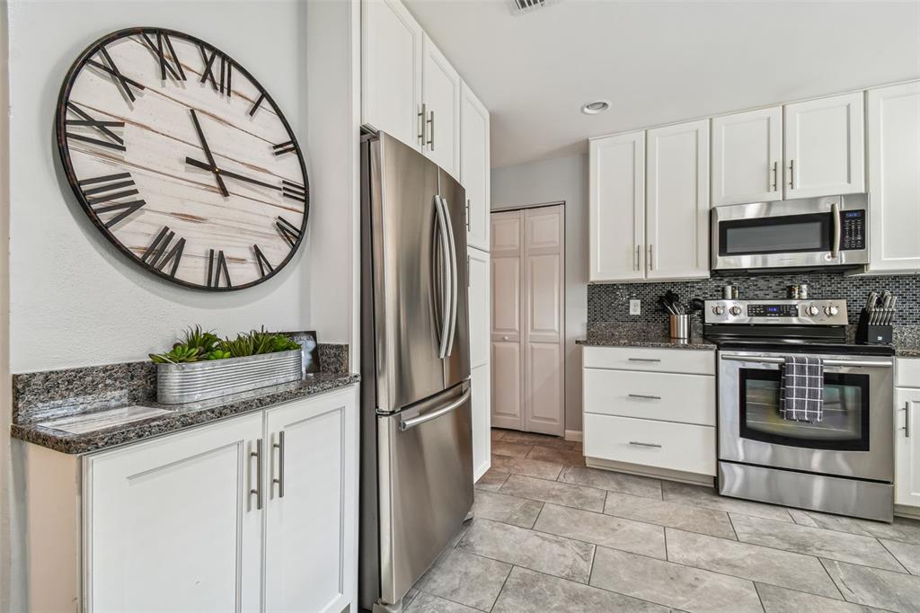 A kitchen features white cabinets, stainless steel appliances, granite countertops, and a large wall clock — 1523 BAYSHORE BOULEVARD UNIT 6, DUNEDIN, FL