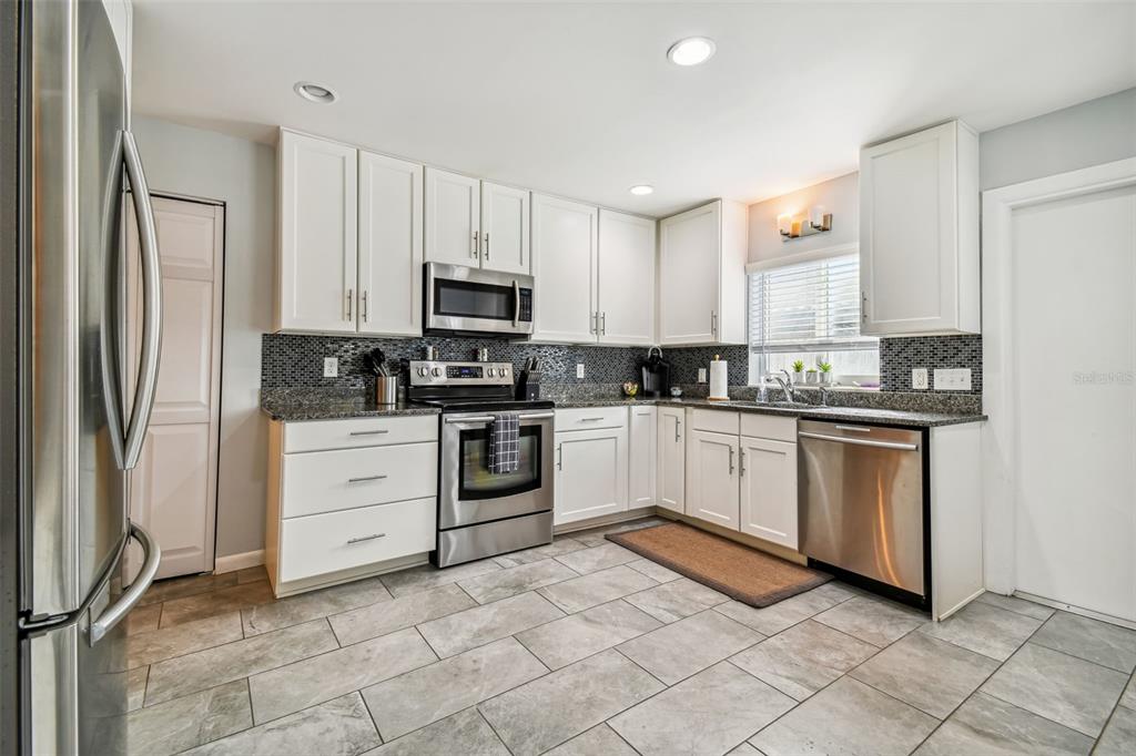A kitchen with white cabinets, stainless steel appliances, granite countertops, and gray tiled flooring — 1523 BAYSHORE BOULEVARD UNIT 6, DUNEDIN, FL