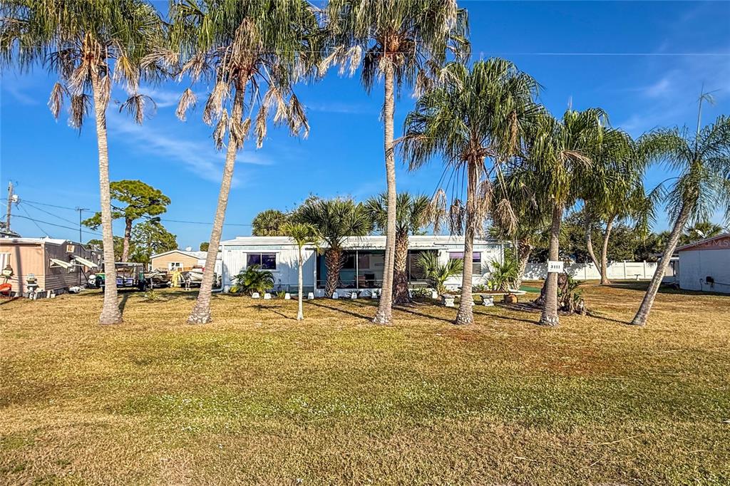 A single-story mobile home with a screened porch is surrounded by palm trees and grass — 3111 WATERSIDE DRIVE, ENGLEWOOD, FL