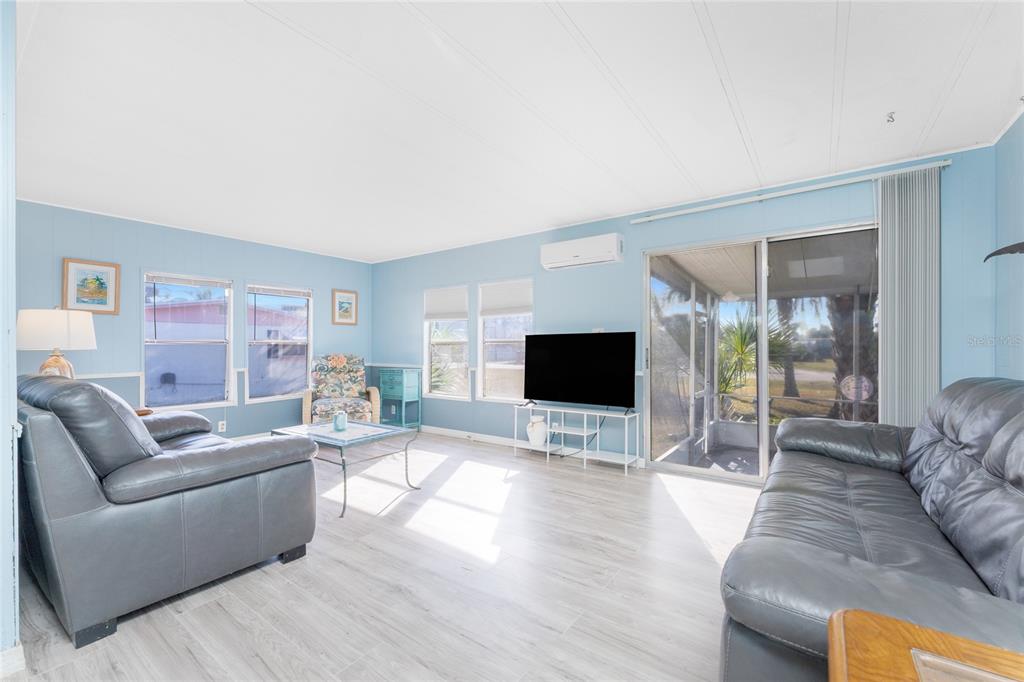A living room features light blue walls, grey leather sofas, and light wood-look flooring — 3111 WATERSIDE DRIVE, ENGLEWOOD, FL