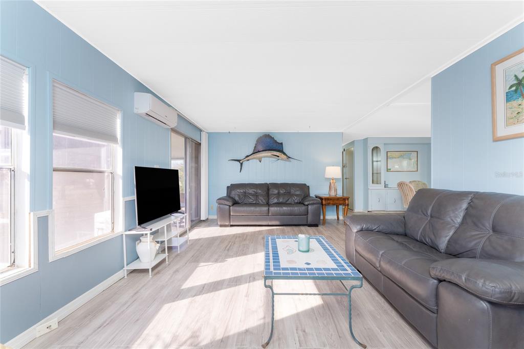 A living room features light blue walls, wood-look flooring, two dark leather sofas, and a television — 3111 WATERSIDE DRIVE, ENGLEWOOD, FL