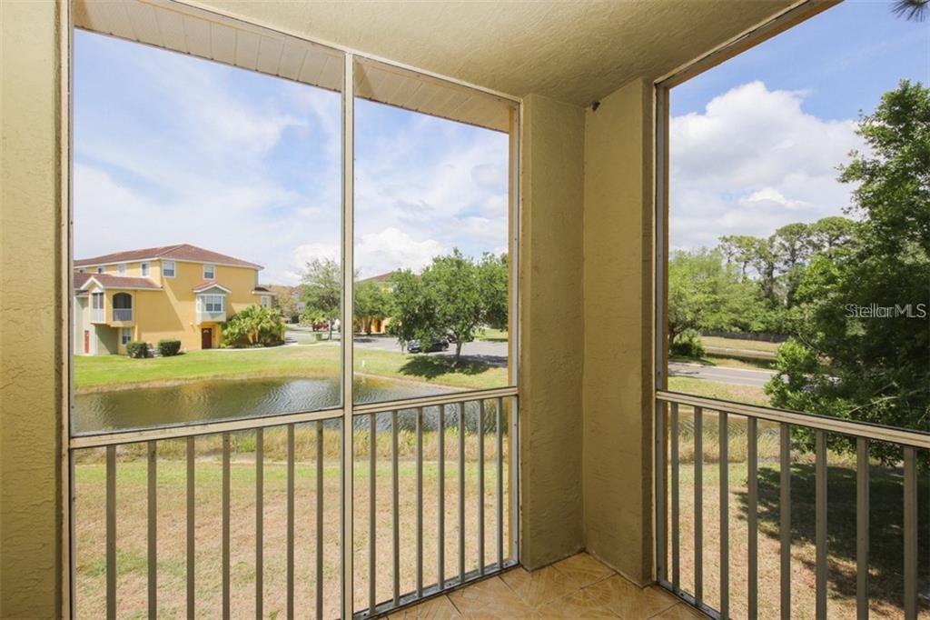 A screened-in balcony with tile flooring overlooks a pond and a neighboring apartment building — 5655 BENTGRASS DRIVE UNIT 9-117, SARASOTA, FL