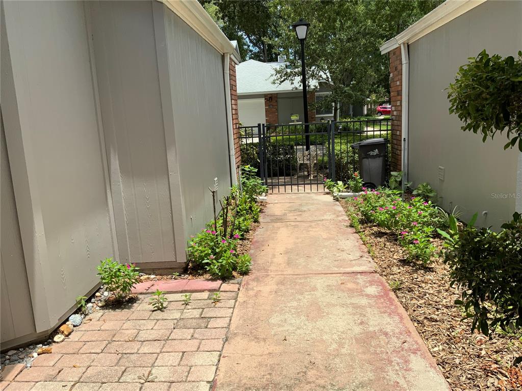 A concrete walkway leads between two building walls toward a metal gate and yard — 618 MAPLE OAK CIRCLE UNIT 112, ALTAMONTE SPRINGS, FL