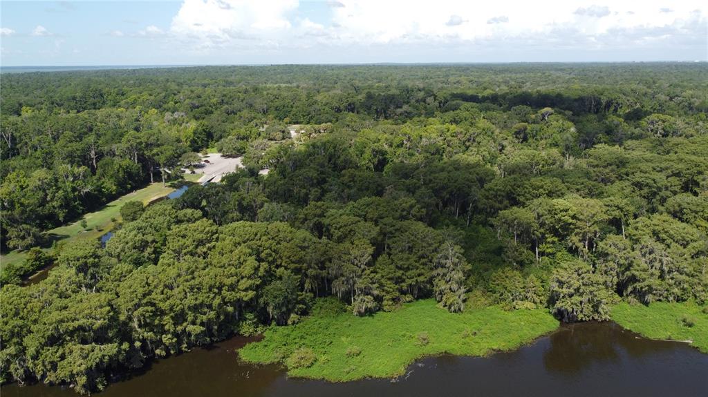 An aerial view shows a dense forest bordering a dark river with a small parking area — SE HAWTHORNE ROAD, GAINESVILLE, FL