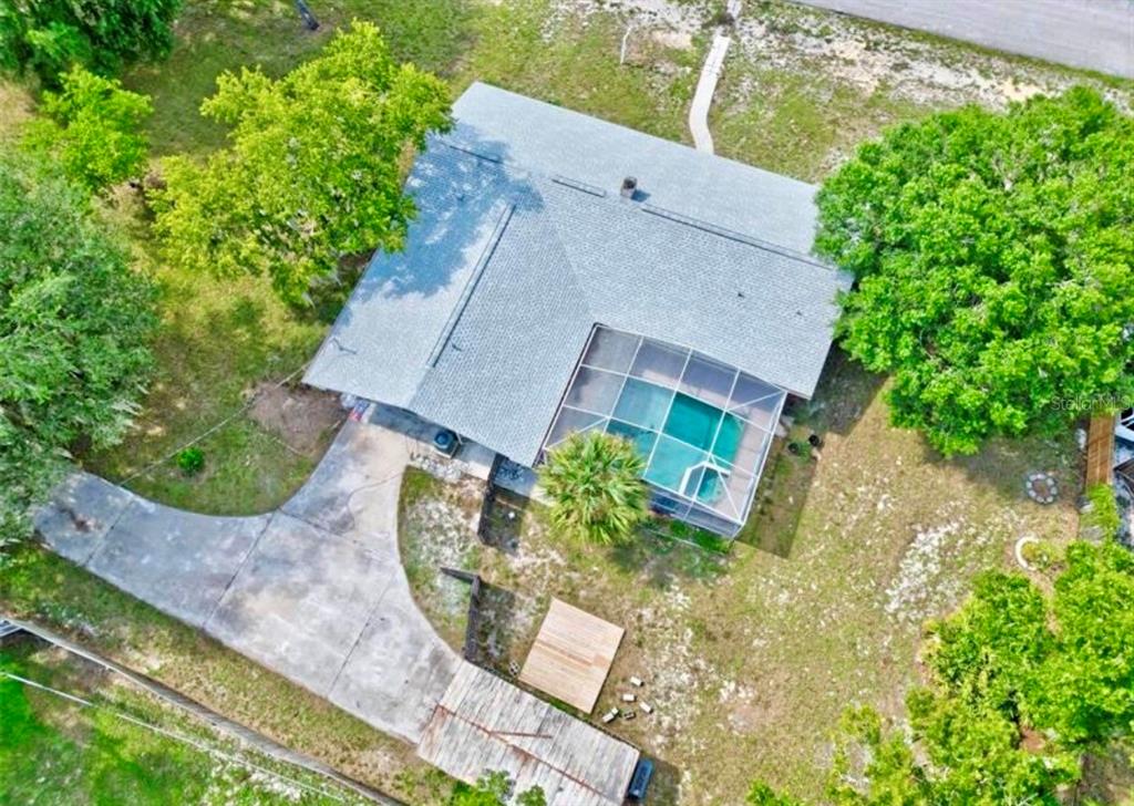 An aerial view shows a house with a screened-in pool, a concrete driveway, and trees — 2831 ASCOT LANE, DELTONA, FL