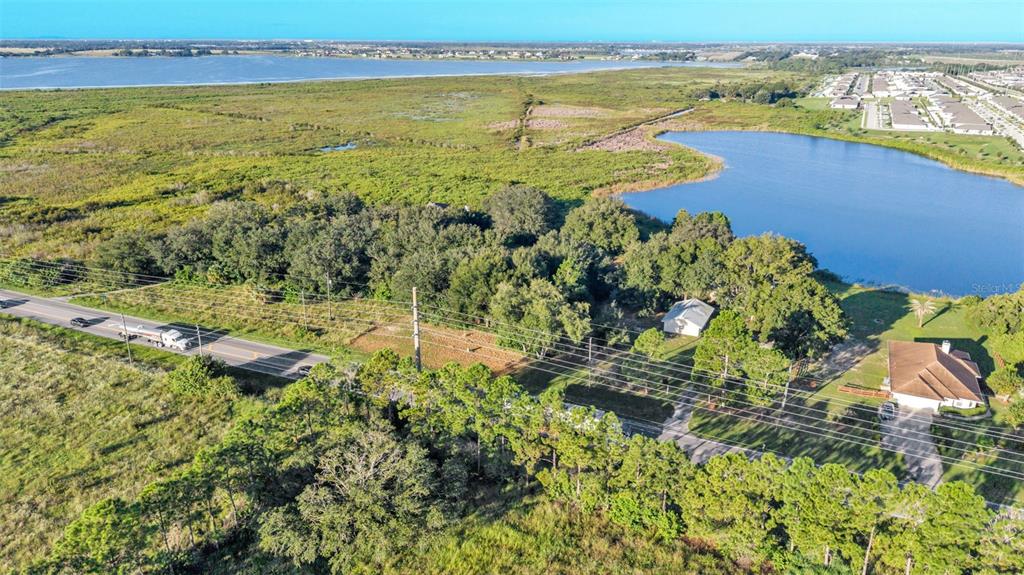 An aerial view shows a road, trees, a lake, and a house with a driveway — HWY 557, LAKE ALFRED, FL